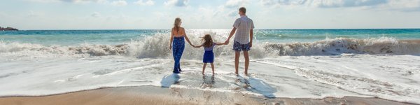 Nainen, lapsi ja mies kävelevät rannalla, jossa UV-säteily on voimakkaampaa.